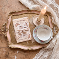 Gold ornate vanity tray with vintage cafe-themed stickers, teacup and candle, baroque cottagecore flat lay